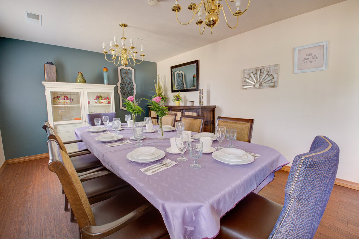 An elegantly set dining room table with a purple tablecloth and decorative elements, complemented by a chandelier and artwork on the walls.