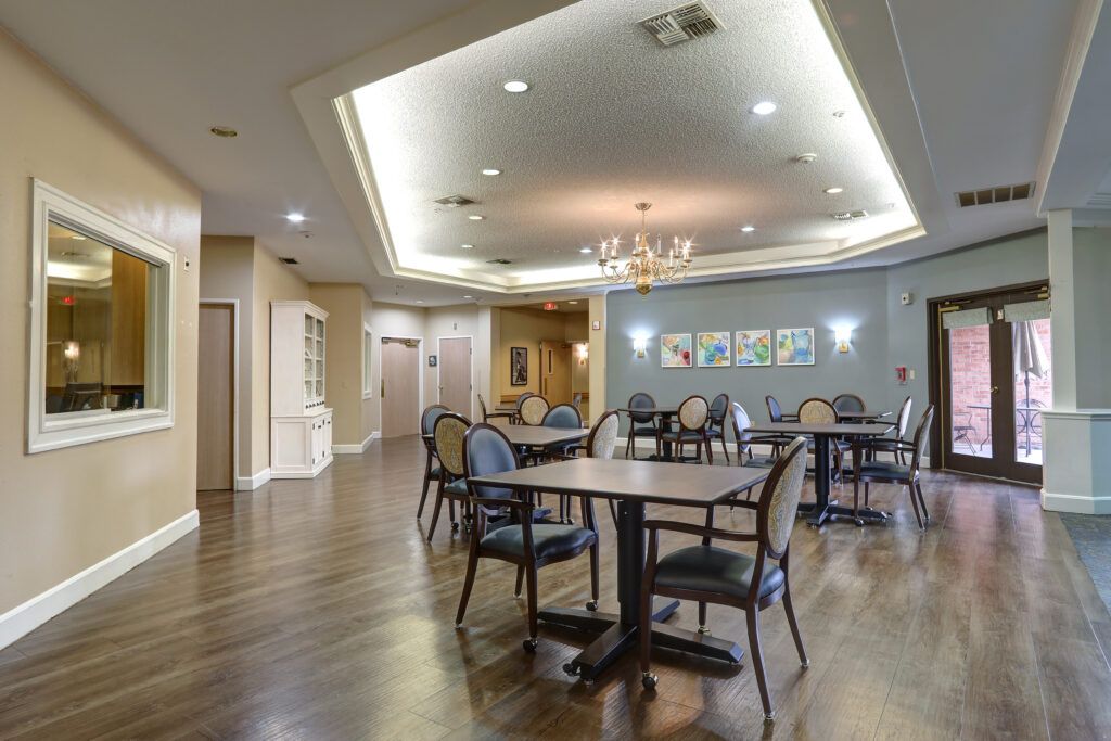 A well-lit dining area with several tables and chairs arranged on polished wooden flooring.