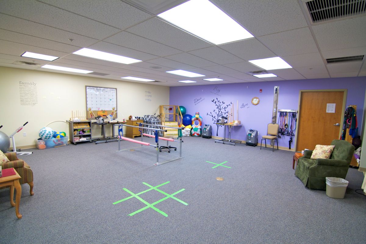 A therapy room equipped with various rehabilitation tools and exercise equipment, featuring floor markings for activities.