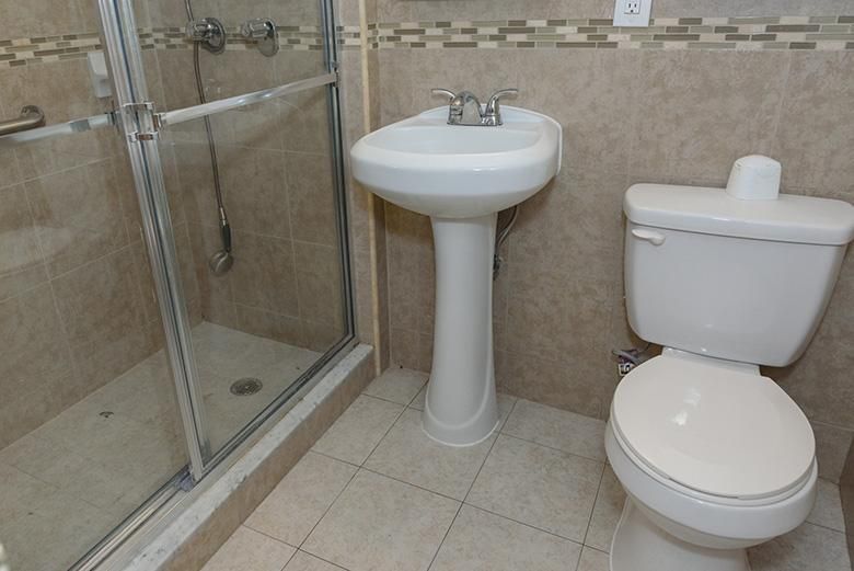 A clean and compact bathroom featuring a pedestal sink, toilet, and glass-enclosed shower.