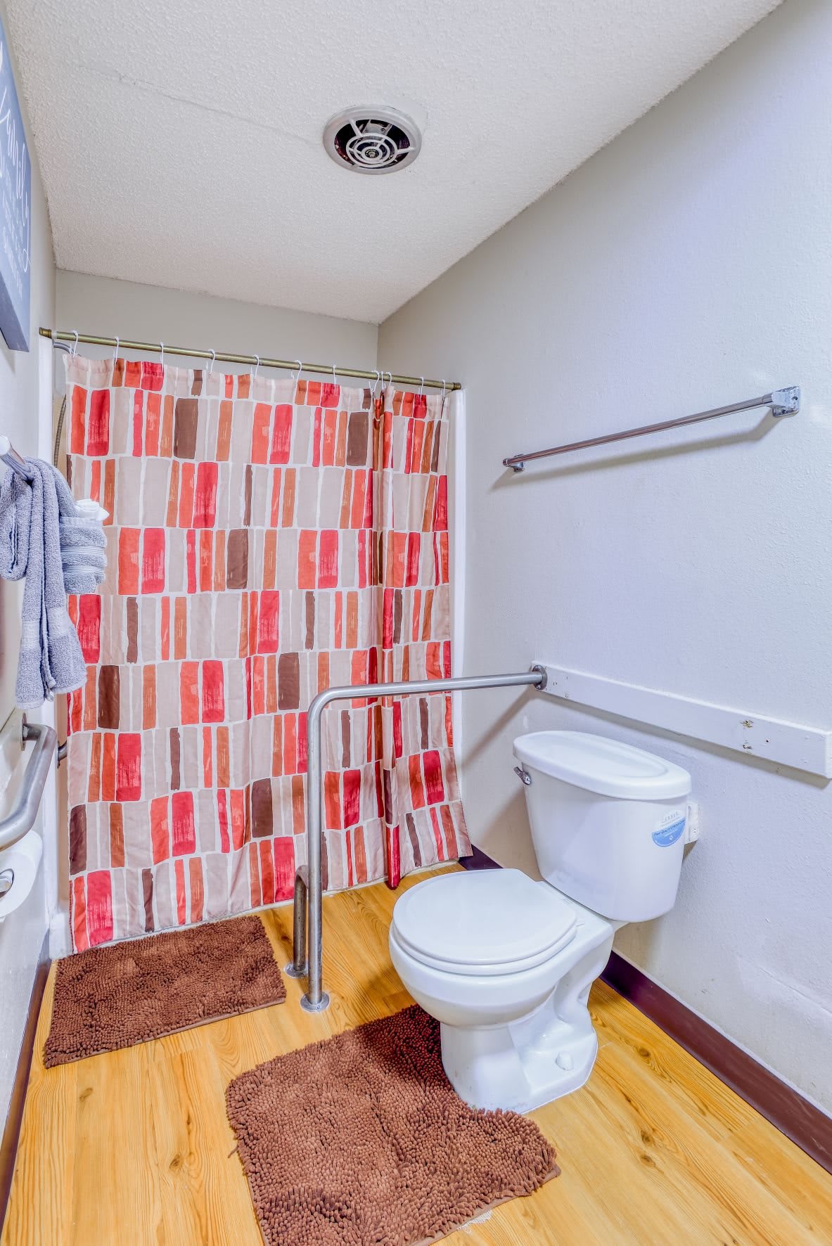 A bathroom with accessibility features, including grab bars and a colorful shower curtain.