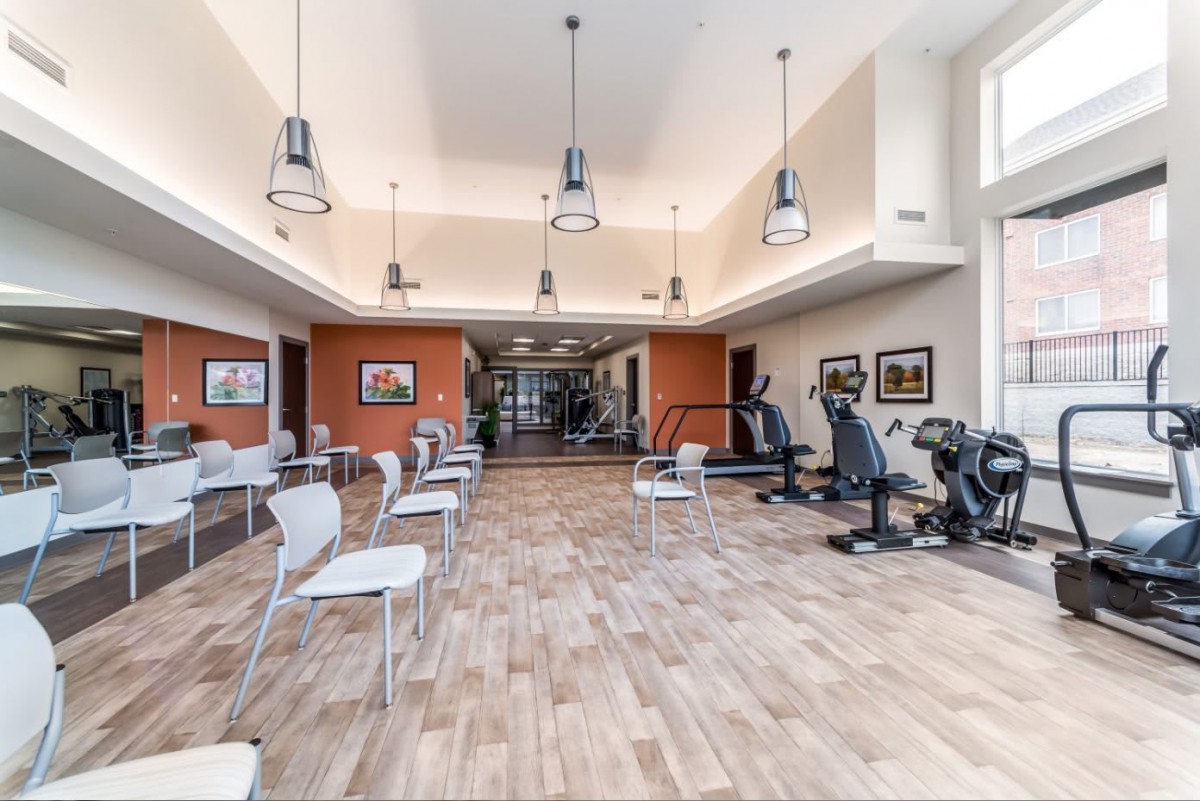 A modern gym with exercise equipment, including treadmills and stationary bikes, set in a spacious area with wood flooring.