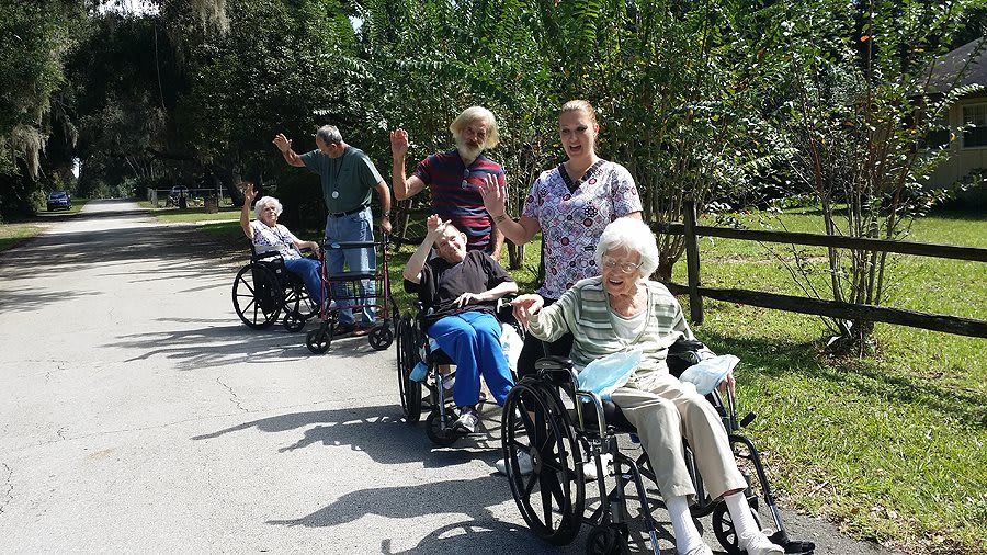 A group of elderly individuals in wheelchairs enjoy a day outside with caregivers.