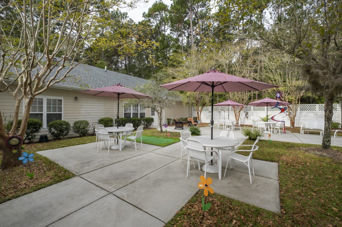 A cozy outdoor patio area with tables and chairs under umbrellas, surrounded by lush greenery.