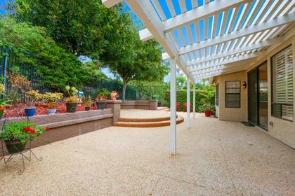 A spacious backyard patio with a pergola and seating area surrounded by lush greenery.