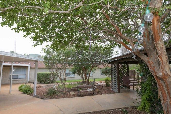 A serene garden area with lush greenery, featuring a gazebo and paved pathway.