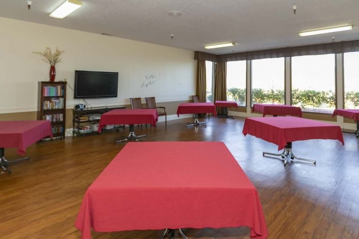 A spacious meeting room with several tables covered in red tablecloths, a television, and a whiteboard.