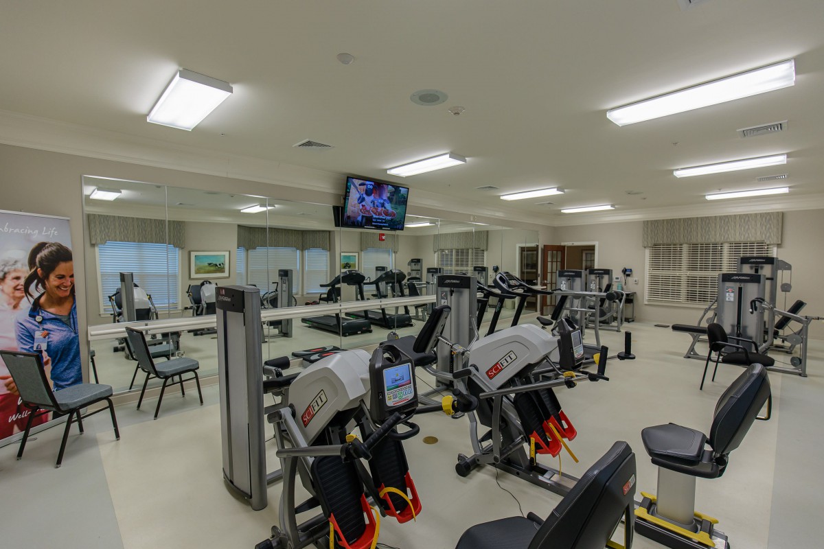 A modern gym with a variety of exercise equipment and a wall-mounted TV.