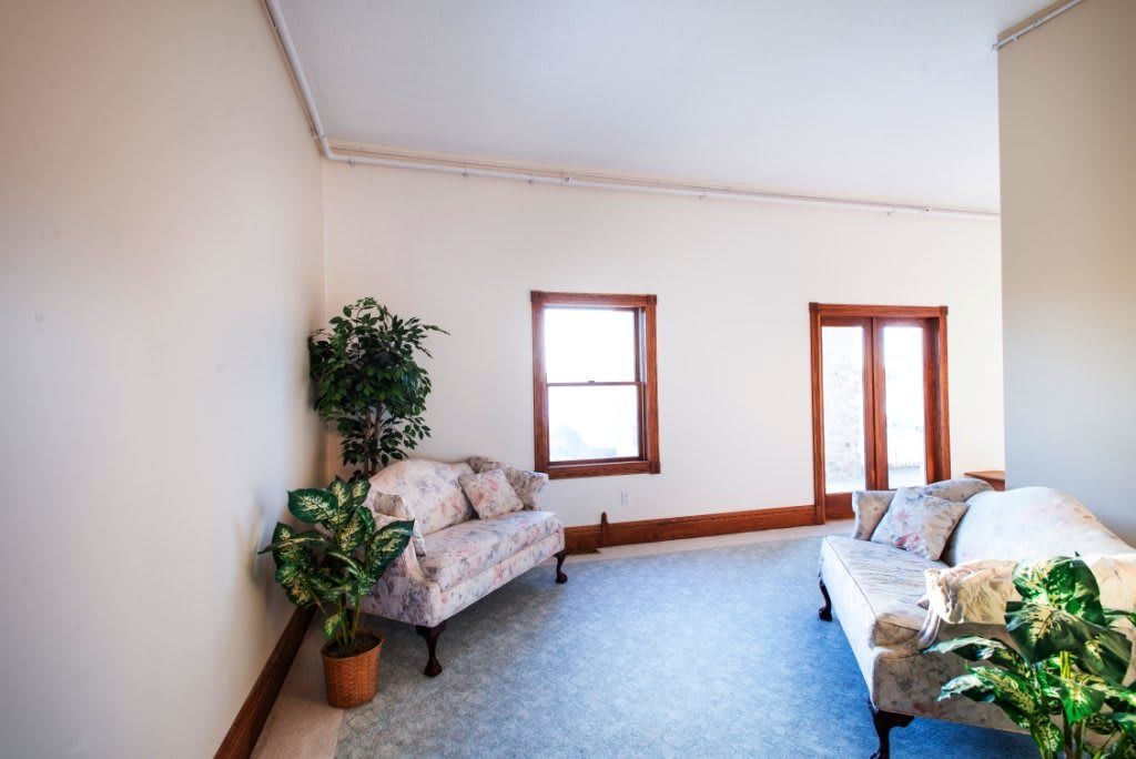 A spacious living room with comfortable seating, indoor plants, and natural light from the windows.