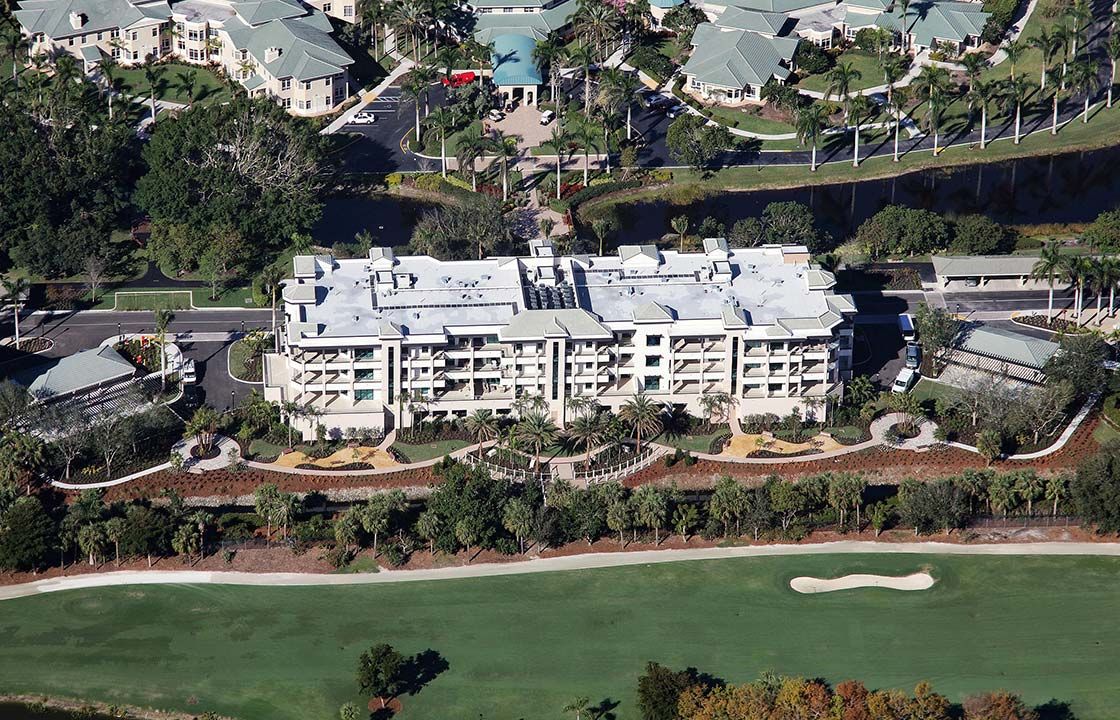 An aerial view of a residential building situated near a golf course and surrounded by landscaped greenery.