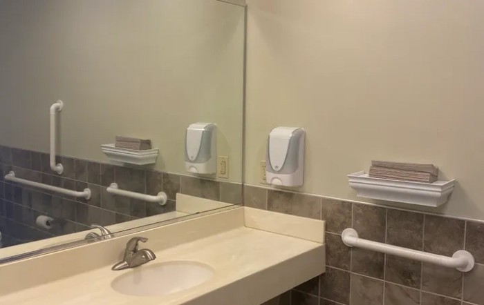 A clean public bathroom sink area with a mirror, soap dispenser, and paper towel dispenser.