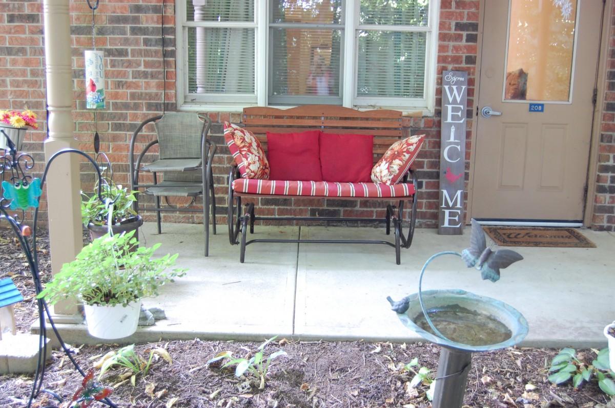 A cozy porch with a bench, red cushions, and decorative elements.