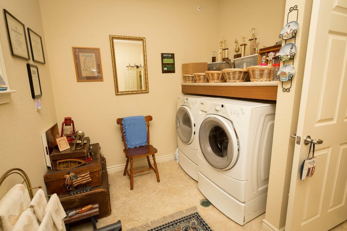 A cozy laundry room featuring a washer and dryer, with decorative elements and a small wooden chair.