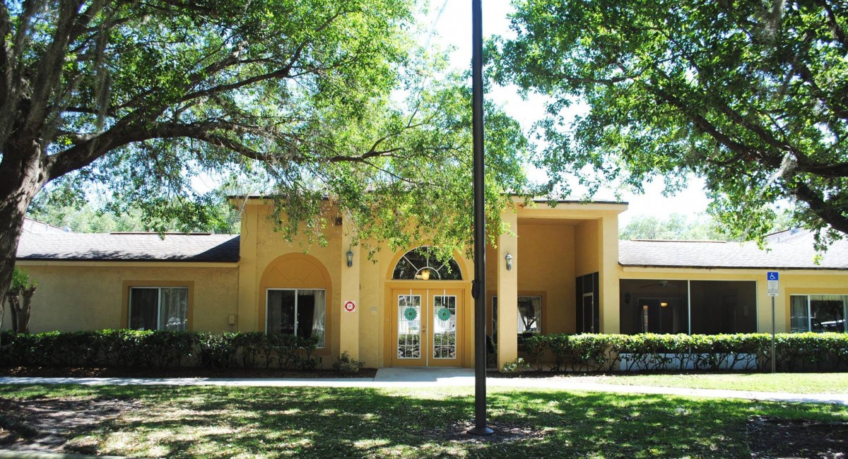 A sunny day view of a yellow building with an arched entrance surrounded by trees.