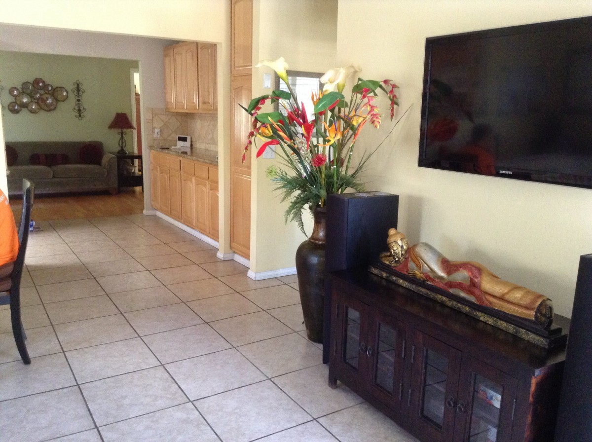 A modern living room with a large television, decorative vase with flowers, and tiled flooring.