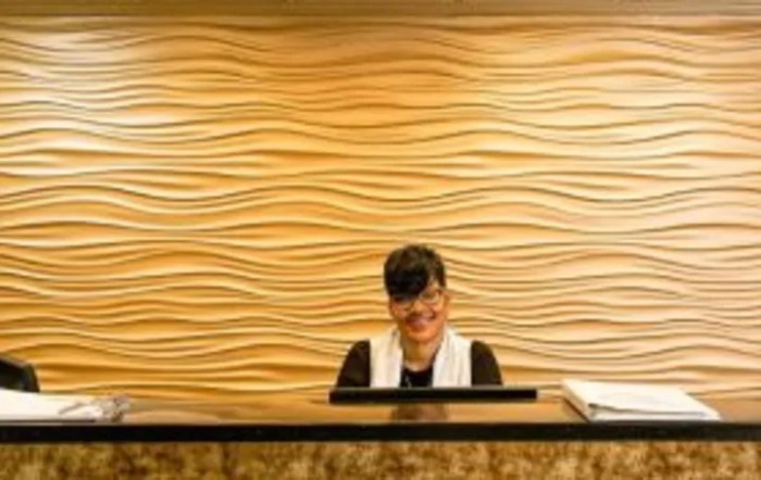 A receptionist working at a desk with a wave-patterned wall in the background.