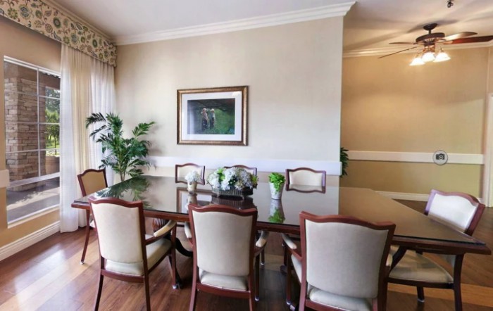 A well-decorated dining room featuring a polished wooden table, elegant chairs, a potted plant, and framed artwork on the wall.