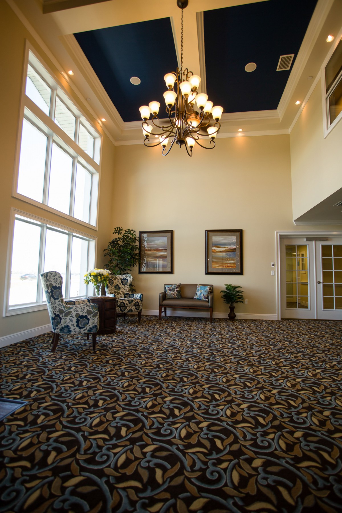 A spacious lobby with a large chandelier, patterned carpet, and decorative artwork on the walls.