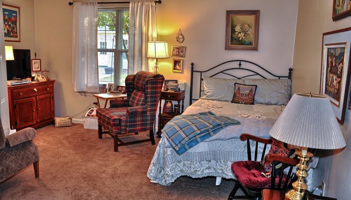 A cozy bedroom with a bed, a plaid armchair, and a lamp by the window.