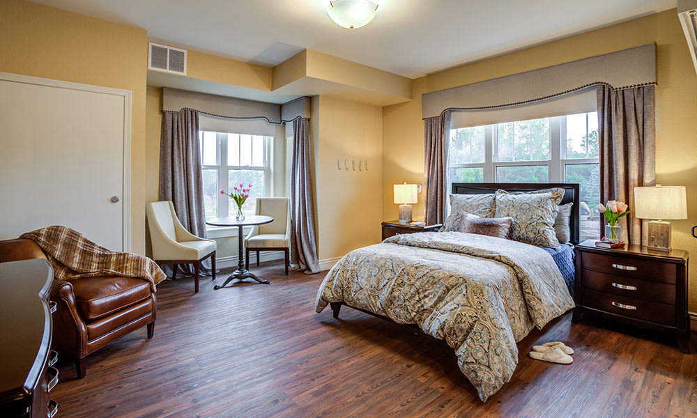 A cozy bedroom with elegant decor, featuring large windows and wood flooring.