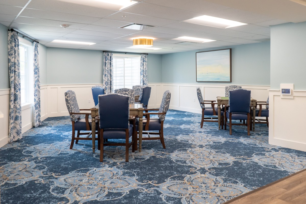 A well-lit dining room with blue carpet and upholstered chairs around wooden tables.