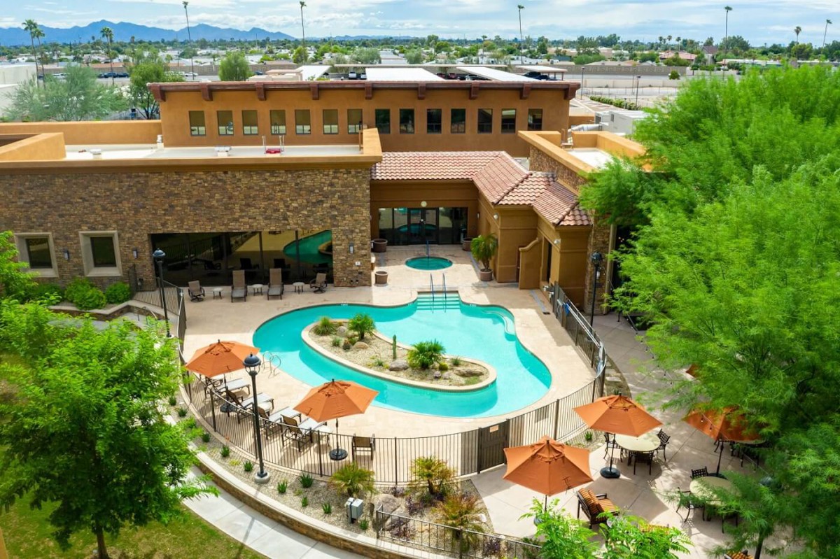 An outdoor swimming pool at a resort, surrounded by trees and umbrellas.