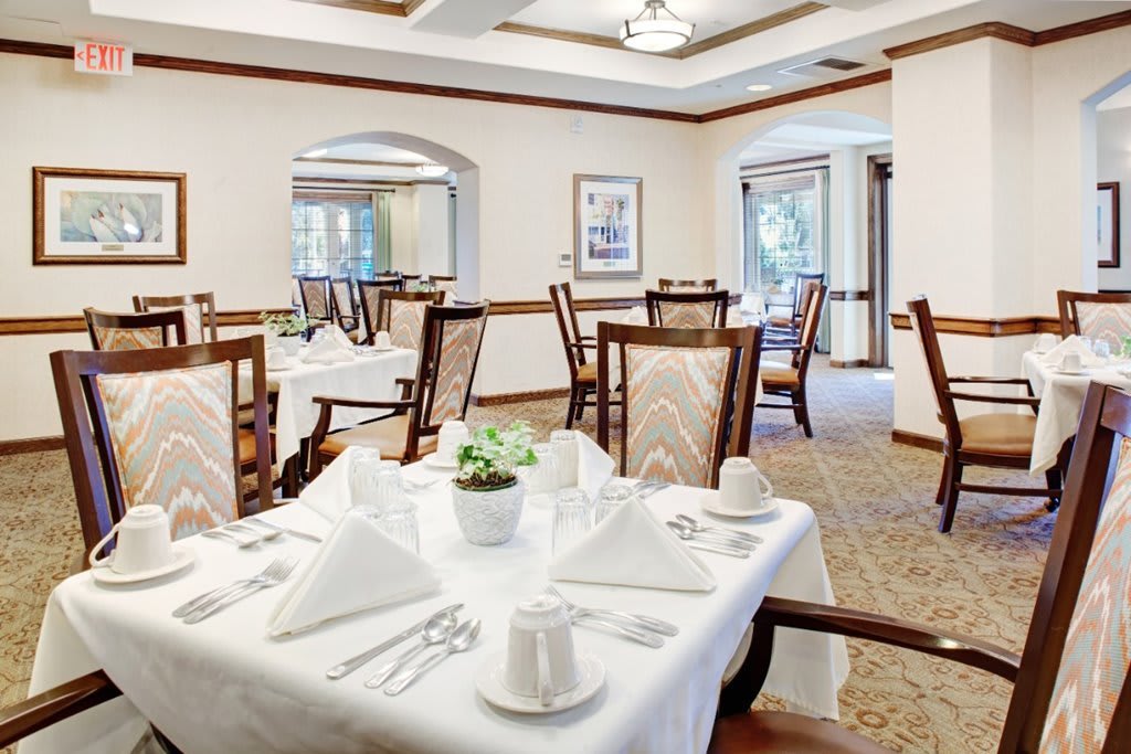 An elegant dining room with neatly arranged tables and chairs, featuring a formal table setting with white tablecloths.