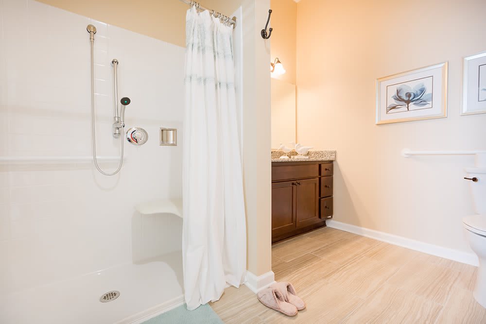 A clean and modern bathroom featuring a shower with a white curtain, a wooden vanity with a mirror above, and light wood flooring.