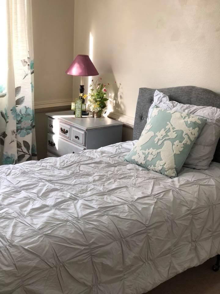 A cozy bedroom with a neatly made bed, decorative pillows, and a nightstand with a lamp.