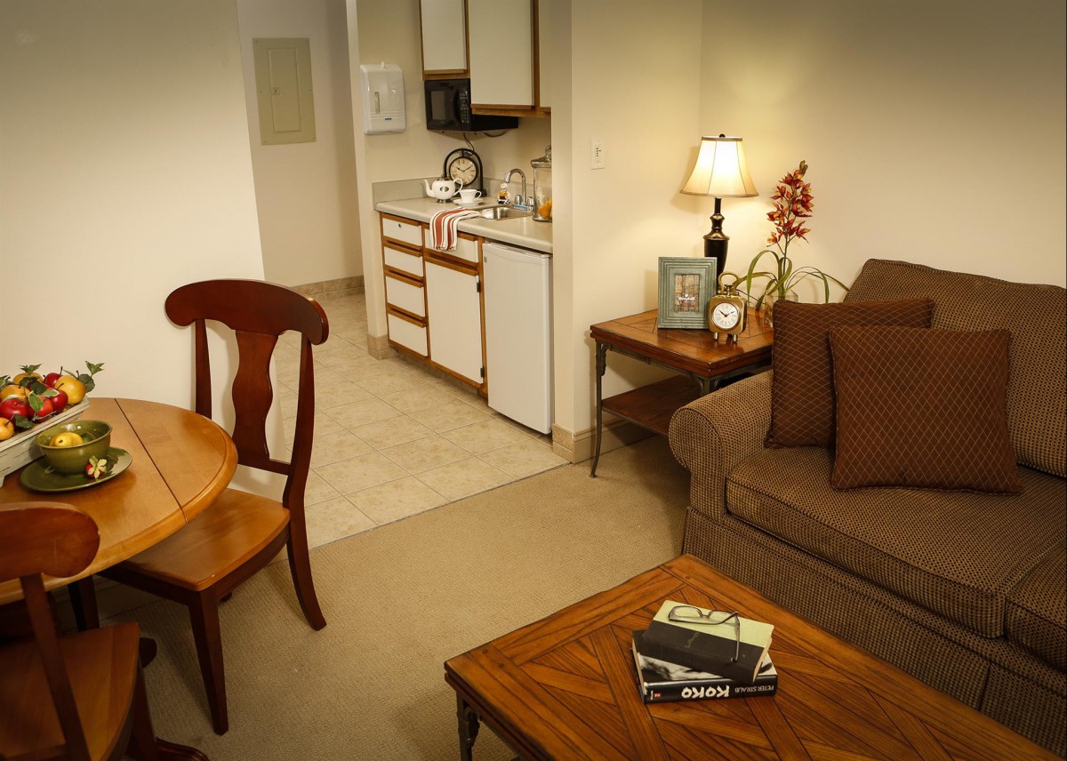 A cozy living space with an adjoining kitchen, featuring a sofa, table, and warm lighting.