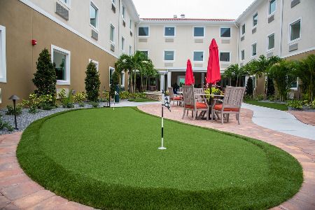 A hotel courtyard featuring a putting green and outdoor seating with red umbrellas.