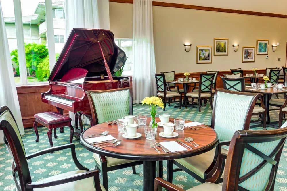 An elegant dining area featuring a grand piano and a neatly set table adorned with flowers.