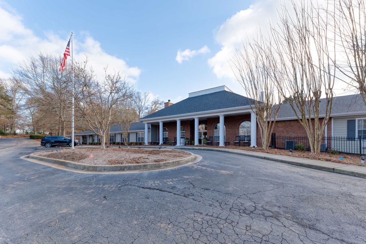 A brick building with a covered entrance and an American flag on display, surrounded by trees.