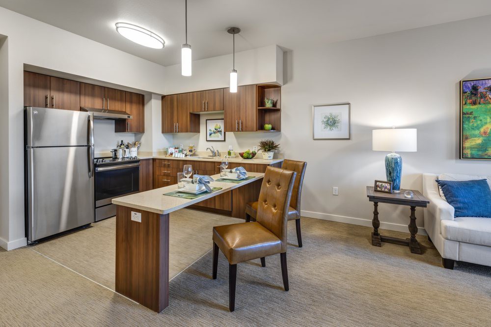 A modern kitchen and dining area with wooden cabinetry, a small dining table with upholstered chairs, and contemporary decor.