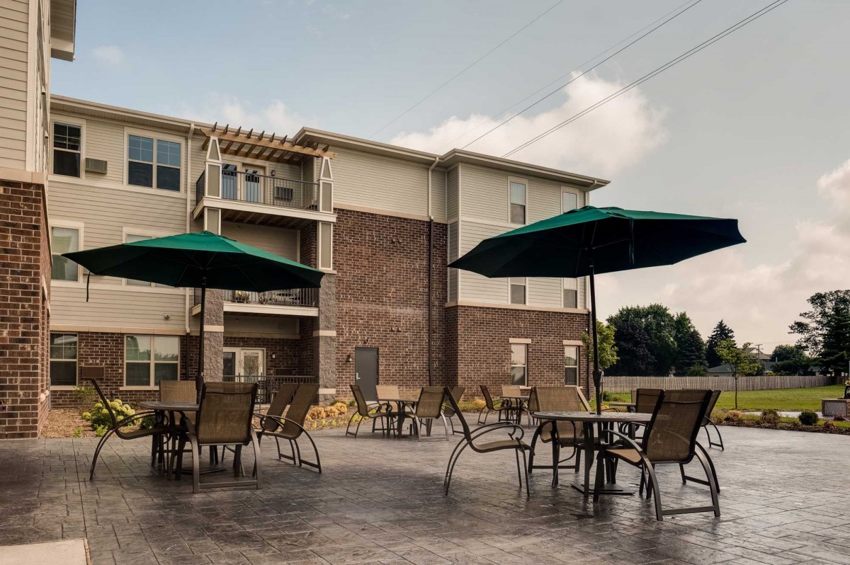 Outdoor patio area with tables, chairs, and umbrellas adjacent to a multi-story building.