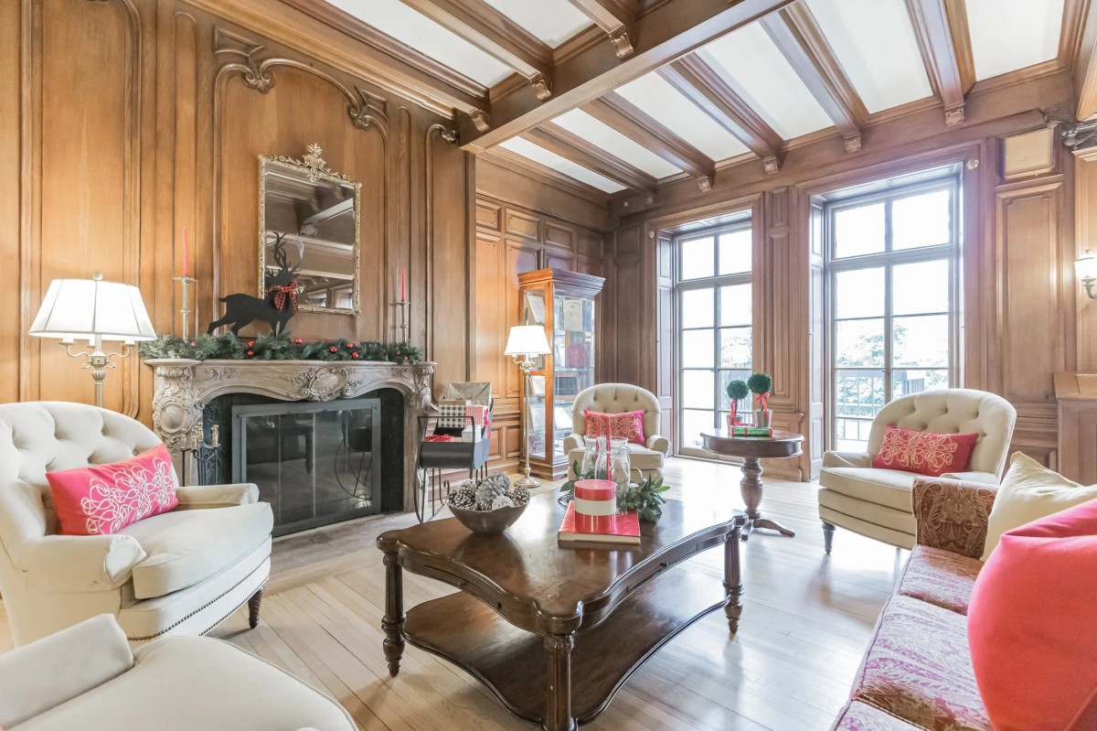 A traditional living room with wood paneling, a fireplace, and ample natural light from large windows.
