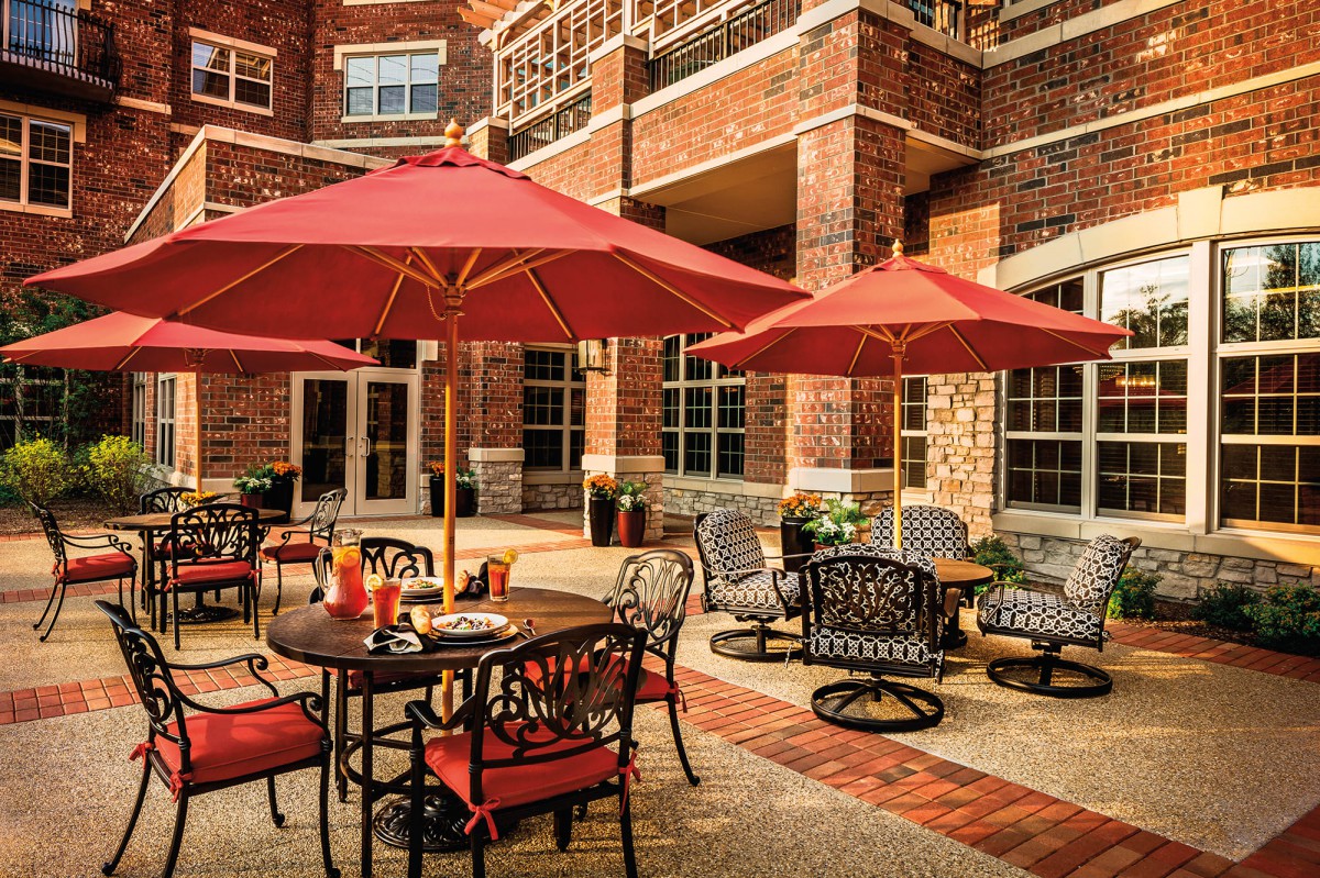 An inviting outdoor patio area with tables, chairs, and red umbrellas set against a brick building.
