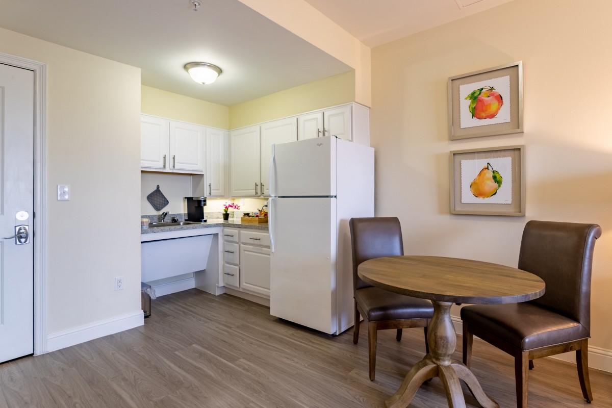 A small kitchen area with white cabinets and a dining table with chairs.