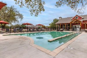An outdoor swimming pool area with lounge chairs and umbrellas, set against a backdrop of trees and a clear sky.