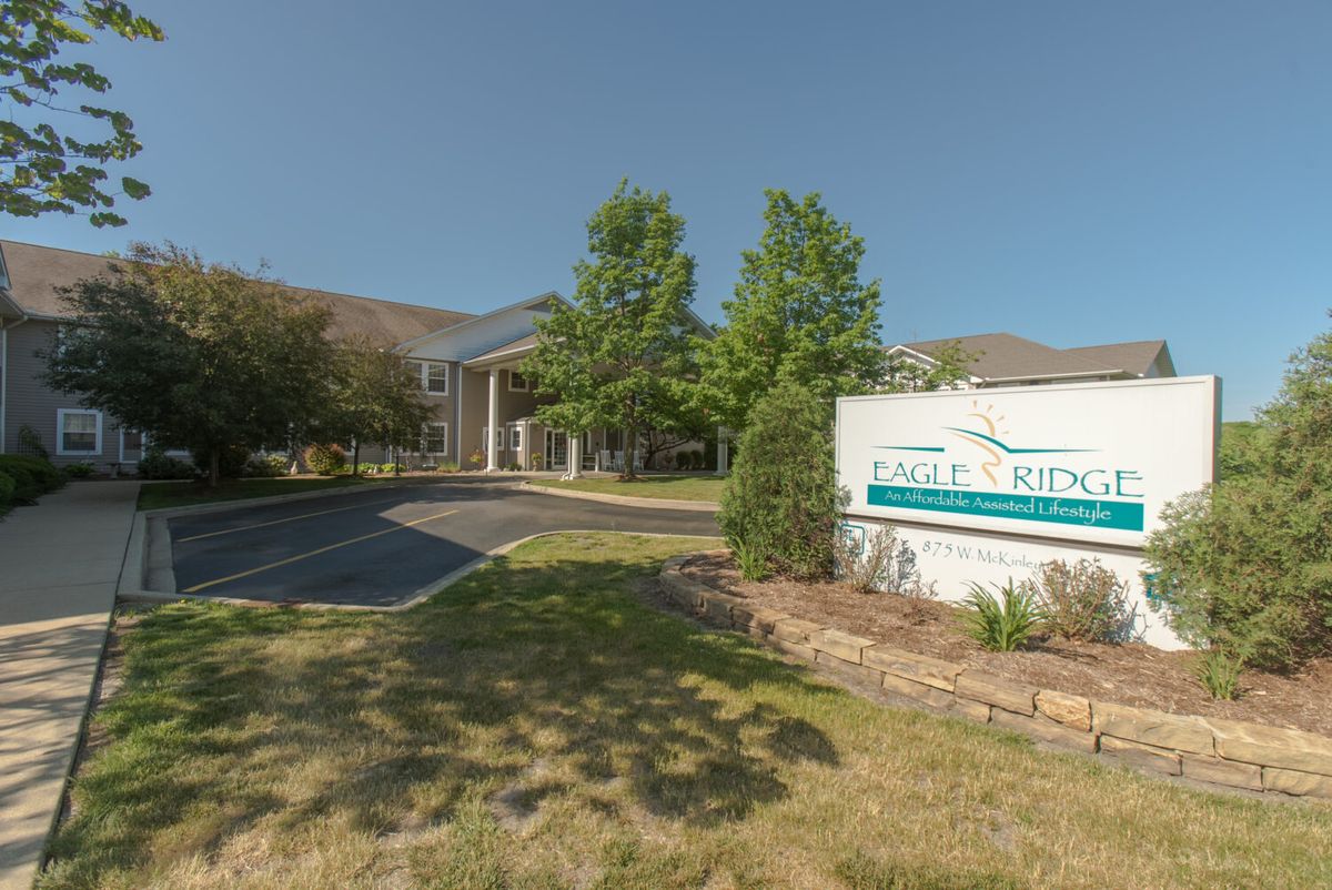 A landscaped driveway leading to a building entrance with a sign nearby.
