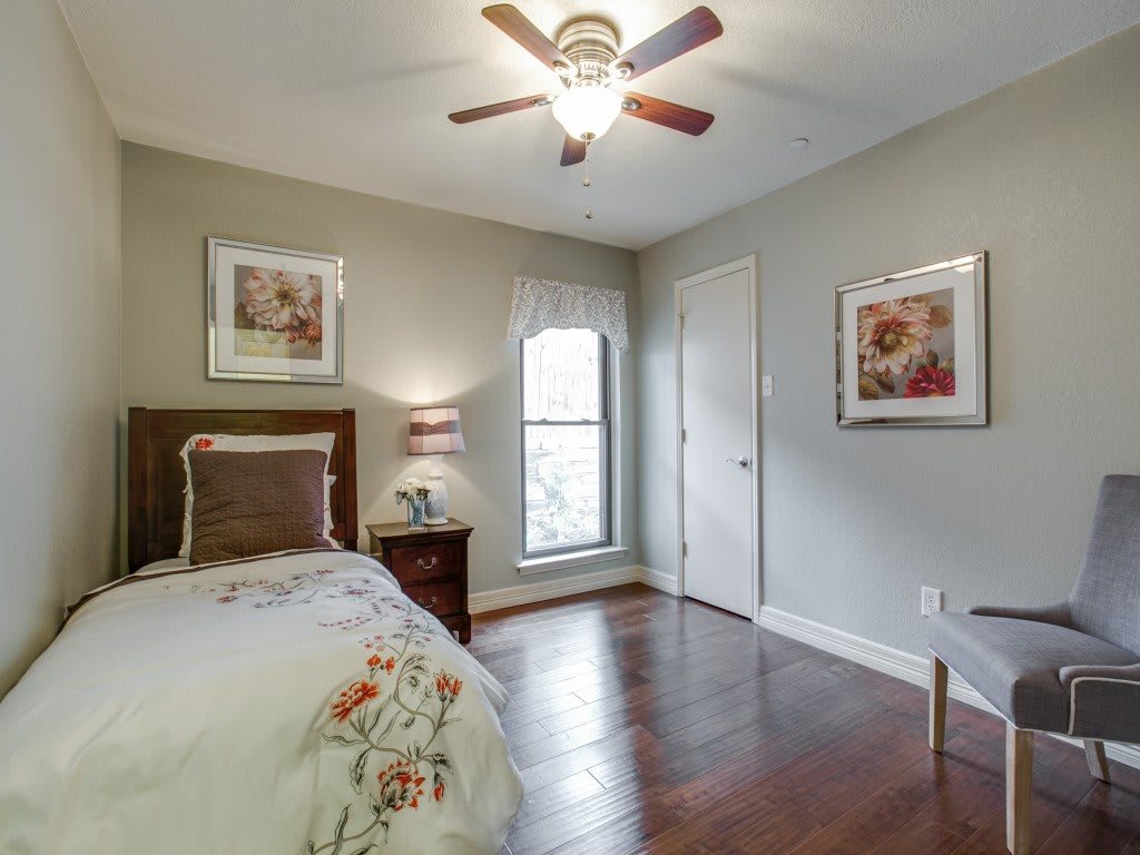 A cozy bedroom with a single bed, adorned with decorative pillows and art on the walls, featuring a ceiling fan and a window for natural light.