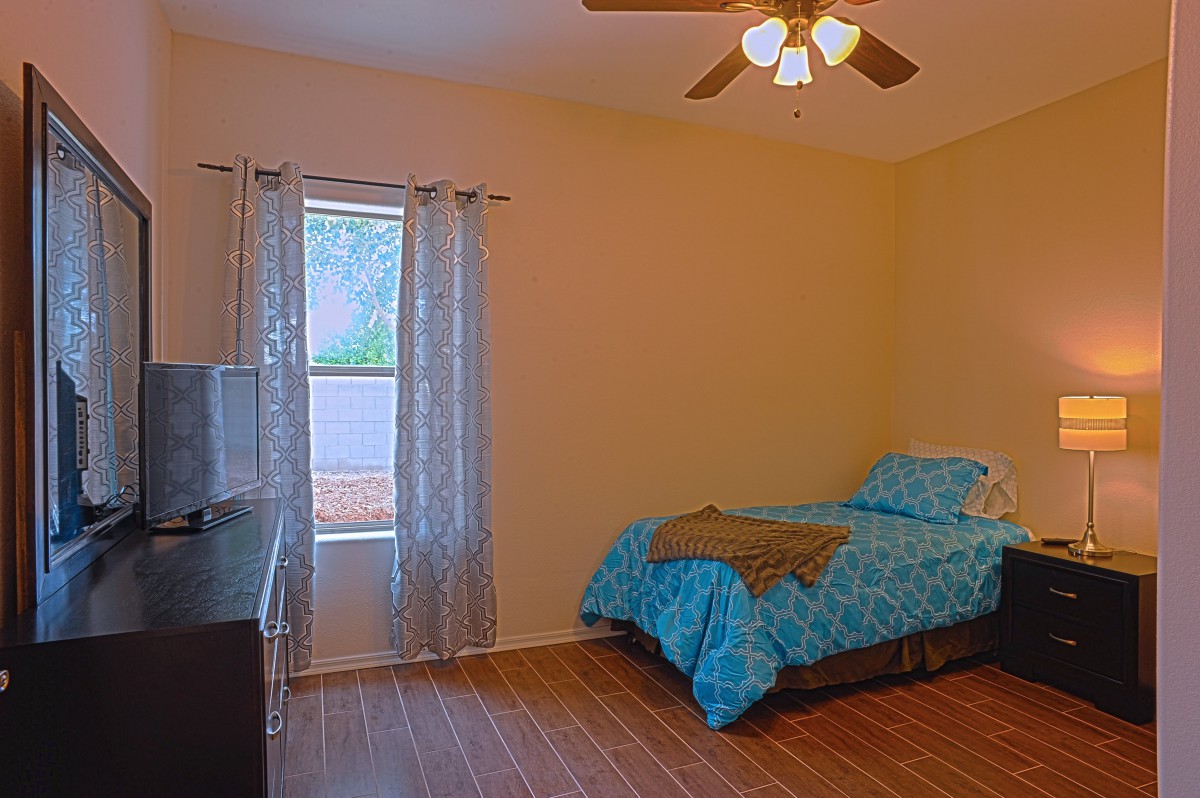 A simple bedroom with a single bed and blue bedding, featuring a ceiling fan and wooden flooring.