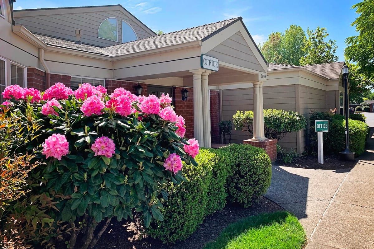 A charming house exterior with vibrant pink flowers and neatly trimmed bushes.
