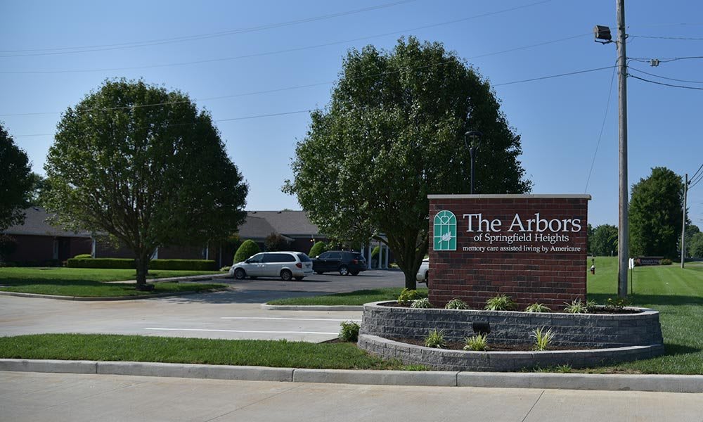 Entrance sign for 'The Arbors' with a landscaped driveway and trees.
