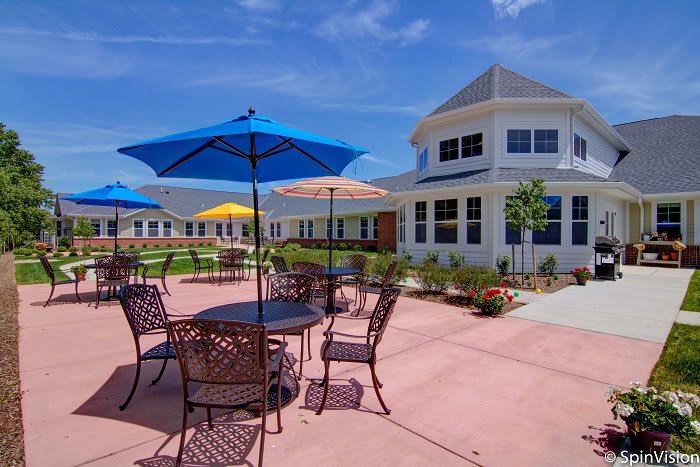 A sunny outdoor patio with tables, chairs, and colorful umbrellas in front of a large building.