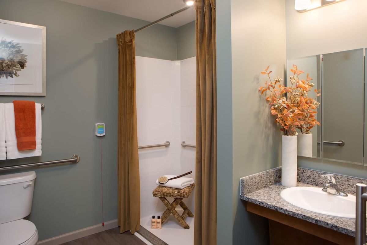 An accessible bathroom with a shower equipped with handrails and a wooden bench, featuring decorative flowers on the countertop.