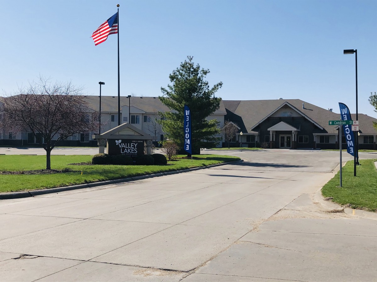 A building with an American flag stands beside a road and parking lot under a clear blue sky.