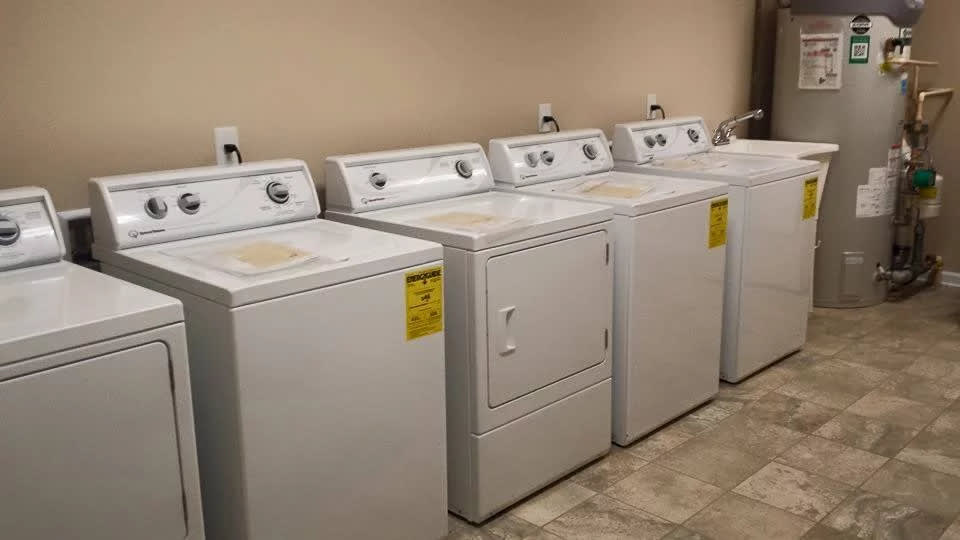 A row of washers and a dryer in a laundry room.