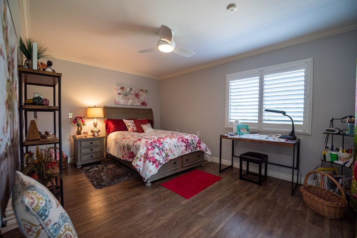 A cozy bedroom with a floral-themed bedspread, side lamp, and work desk.