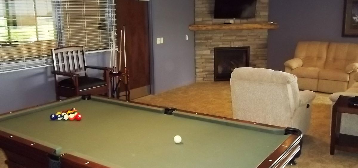 A cozy living room with a billiard table, pool cues, fireplace, and a television.